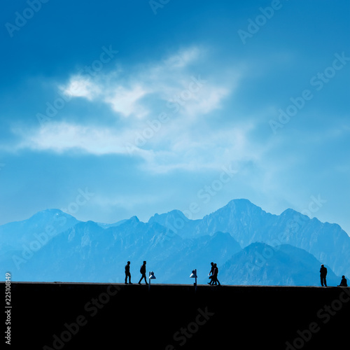 Silhouetted people walking on street over blue sky