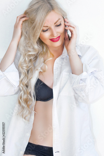 Beautiful young blonde in an unbuttoned male shirt and in lingerie, smiling beautifully.