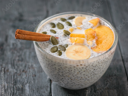 Chia seed pudding with peach, pumpkin seed and cinnamon on a dark wooden table.