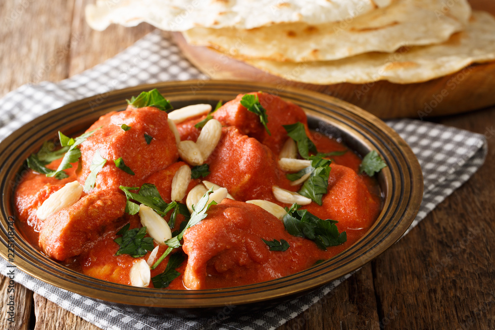 Indian popular food Butter Chicken Murgh Makhani with spicy sauce, almonds and cilantro close-up on a plate with bread roti on the table. horizontal Indian popular food Butter Chicken Murgh Makhani with spicy sauce, almonds and cilantro close-up on a plate with bread roti on the table. horizontal