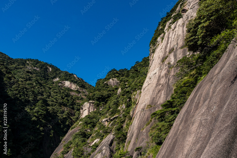 rock face on the mountain top covered in green on a sunny day under blue sky