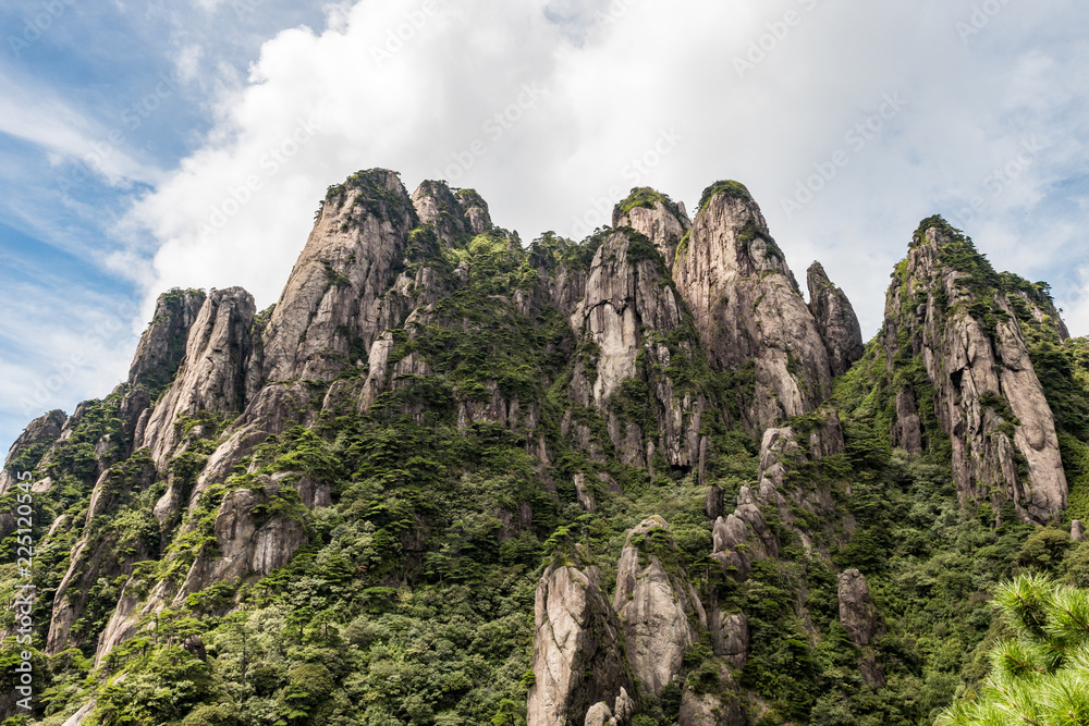 unique rock formation covered with forest on the peaks of Mount Sanqing under the cloudy blue sky
