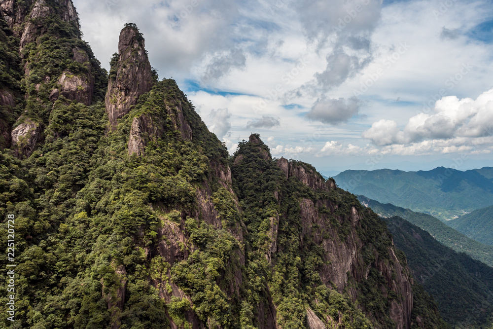 unique rock formation covered with forest on the slope of Mount Sanqing under the cloudy blue sky