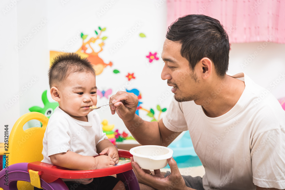 Father acting Mom feeding his son baby 1 year old on chair Father acting Mom feeding his son baby 1 year old on chair