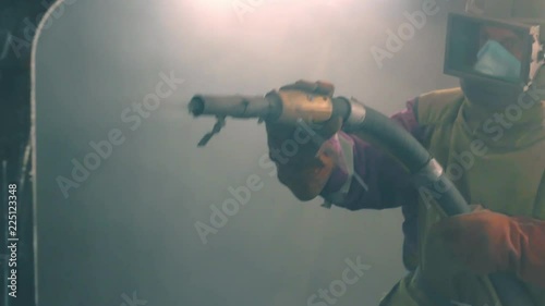 Man cleans metal surface by sandblaster gun in a metal construction factory. Shotblaster in a process