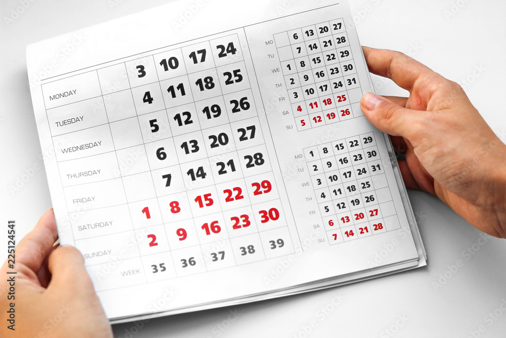 Hand holding the calendar. White calendar. Weekends are highlighted in red. Close up Hand holding the calendar. White calendar. Weekends are highlighted in red. Close up