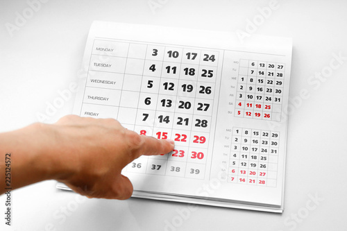 Hand pointing to the calendar. White calendar. Weekends are highlighted in red. Close up