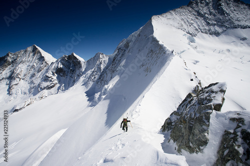 A ski mountaineer traversing a steep snowy ridge in the mountains of the Swiss Alps
