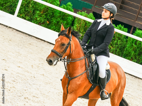 Beautiful girl on sorrel horse in jumping show, equestrian sports. Light-brown horse and young woman in uniform going to jump. 