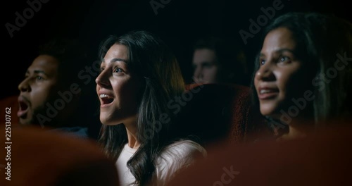 Movie theatre audience watching a movie. Focus on young woman who reacts with amazement during a scene