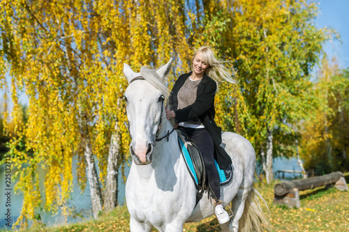 Young blonde woman riding a horse in autumn forest.