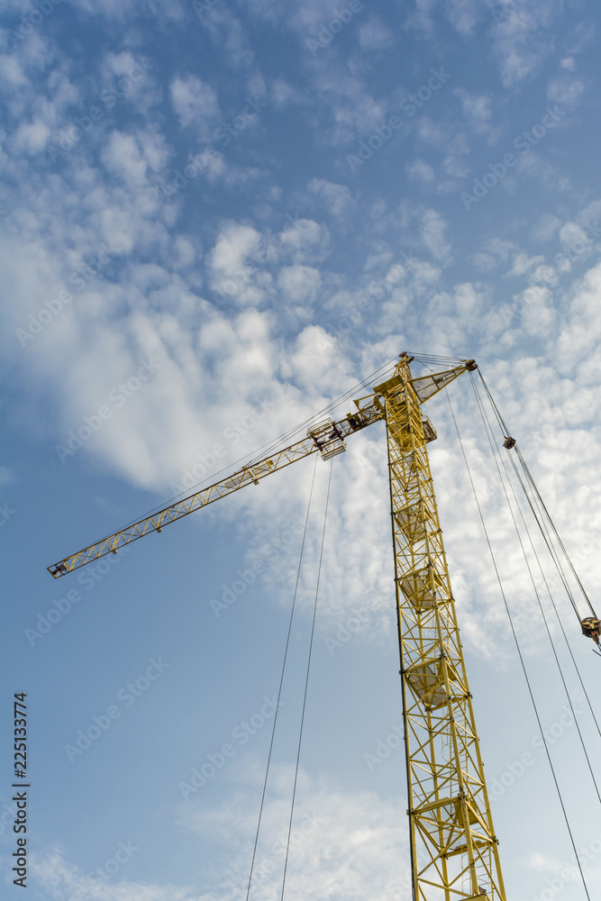 yellow tower crane on a background of blue sky with clouds, industry abstract background