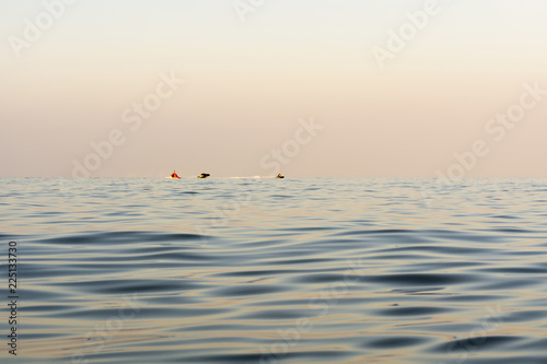 evening sea with waves, far away on a horizon line floating water bike, nature abstract background
