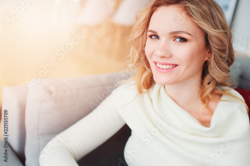indoor portrait of young selfish beautiful woman enjoying time at home, sitting on cozy couch in warm sweater. Happy life, positive thinking, balance and restore concept