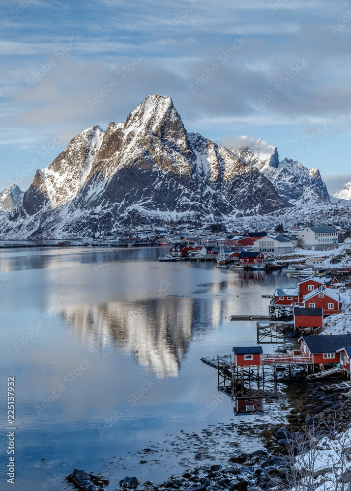 Lofoten Islands, Norway. Winter mountains and fjord with rorbu - typical red fishing lodge, reflection in water. Blue hours. Vertical landscape. Travel Norway.