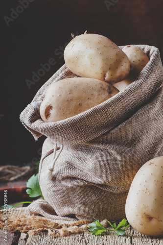 Autumn harvest of potatoes in canvas bag on old wooden table, rustic style, selective focus