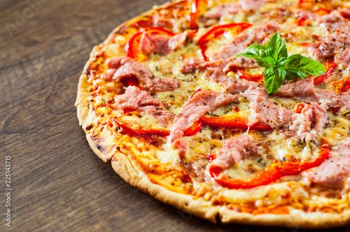 Pizza with Mozzarella cheese, ham, pepper, meat, Tomatoes, Spices and Fresh Basil. Italian pizza on wooden background