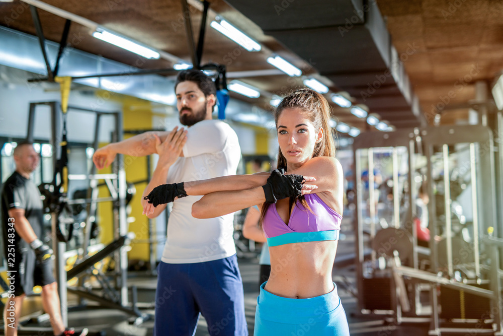 Strong fit young couple stretching their muscles after training in gym.