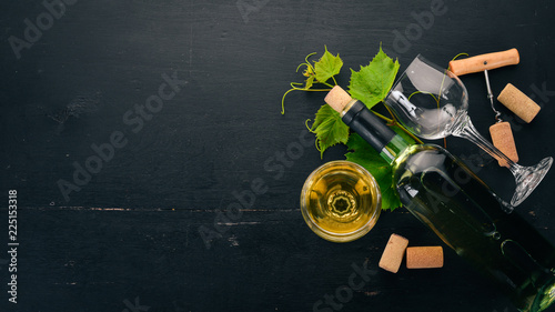 A bottle of white wine with glasses and grapes. Leaves of grapes. Top view. On a black wooden background. Free space for text.