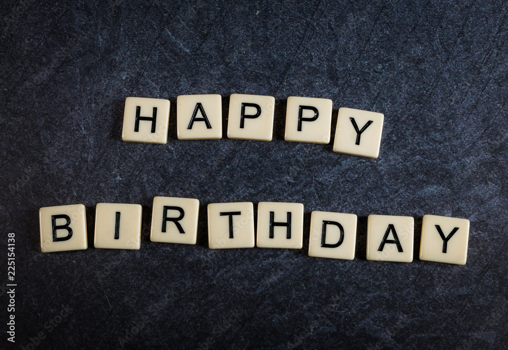 Scrabble letter tiles on black slate background spelling happy birthday Scrabble letter tiles on black slate background spelling happy birthday