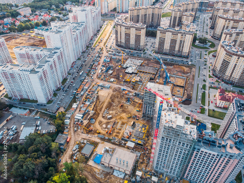 Aerial view from above, construction of modern houses or buildings with cranes and other industrial vehicles among city architecture - obrazy, fototapety, plakaty 