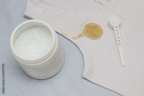 A spot on a white T-shirt, next to it is a container with a stain remover, close-up, bleach