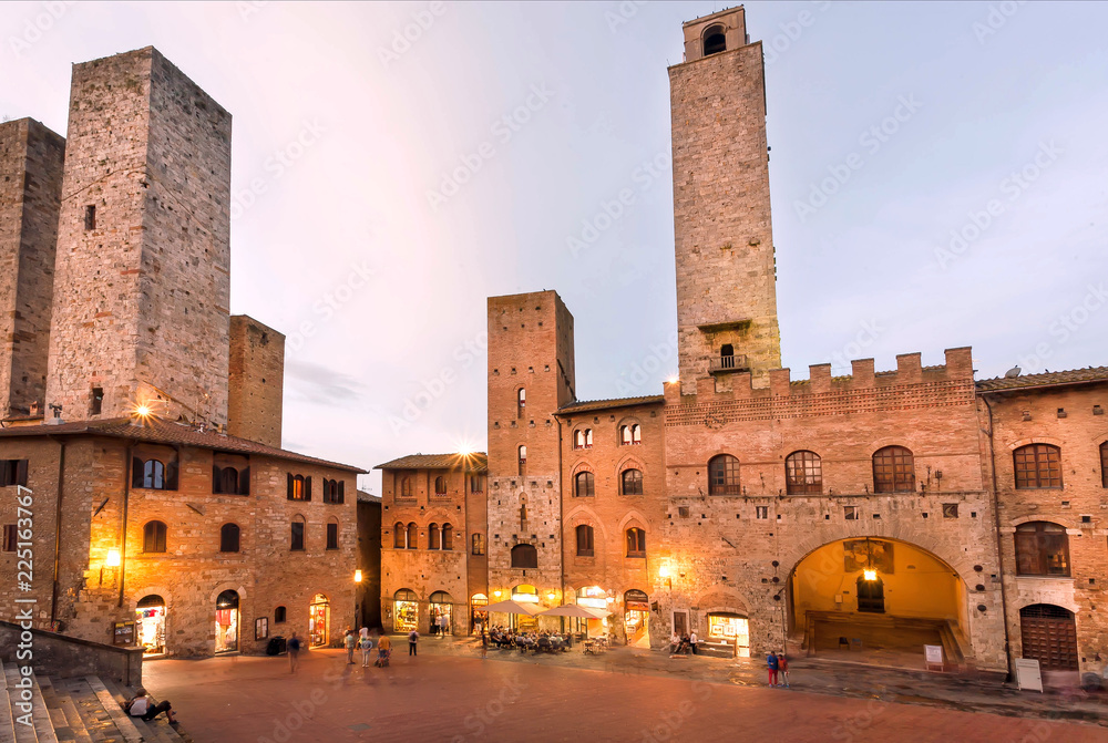 Towers and traditional houses on square of ancient Tuscan town in evening lights