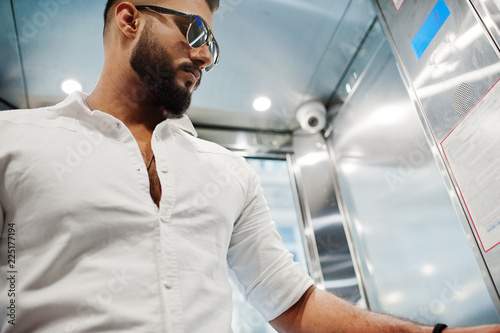 Stylish tall arabian man model in white shirt and sunglasses posed at elevator inside.