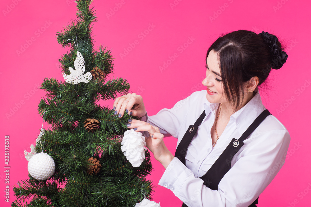 Christmas, holidays and people concept - young happy woman decorating christmas tree on pink background Christmas, holidays and people concept - young happy woman decorating christmas tree on pink background