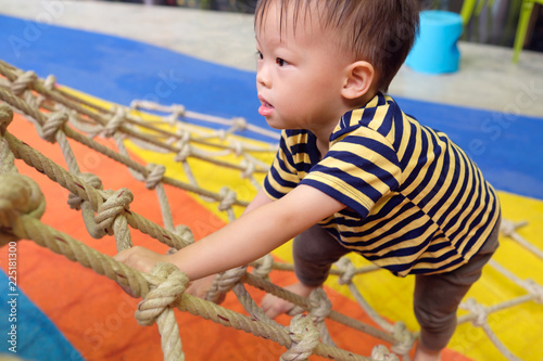 Cute little Asian 2 years old toddler baby boy child having fun trying to climb on jungle gym at indoor playground, Physical, Hand and Eye Coordination, Sensory, Motor Skills development concept