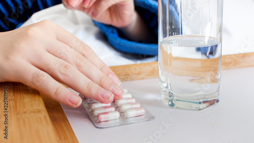 Closeup image of sick woman lying in bed and holding pack of pills