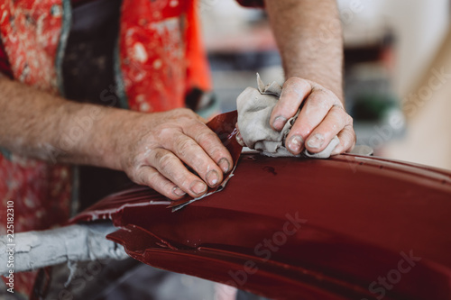 Car detailing - Man with sandpaper in auto repair shop sanding polishing and preparing car parts for painting. Selective focus on man's hand.