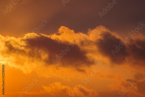 Dramatic view of a dark silhouettes of clouds in the orange sky illuminated by the rising sun © Mikhail