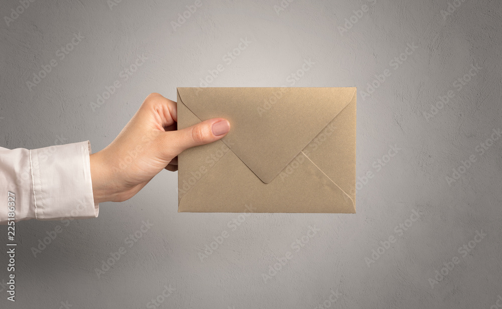 Fototapeta premium Female hand holding coloured and white envelope with empty wall background 