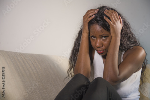 young attractive and sad black African American woman sitting depressed at home sofa couch feeling anxious and frustrated suffering depression problem and headache