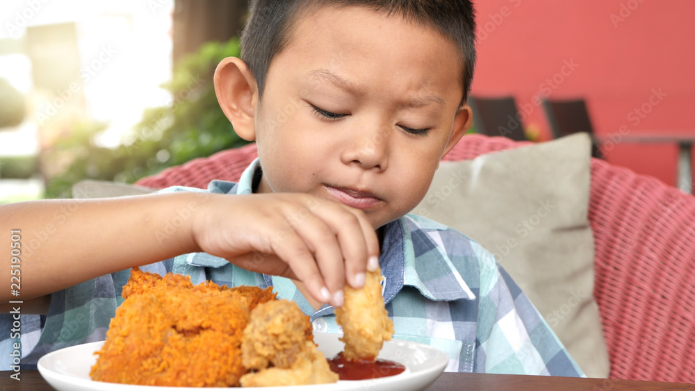Cute asian boy are happy eating fried chicken leg in restaurant Cute asian boy are happy eating fried chicken leg in restaurant