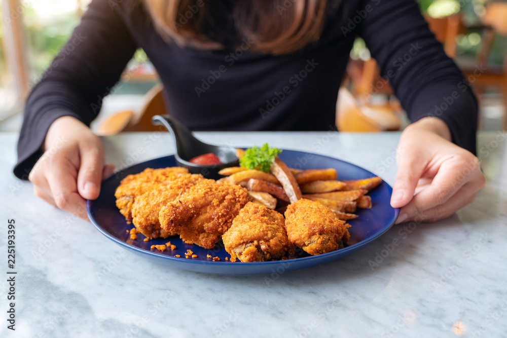 Closeup image of a woman holding a plate of fried chicken and french fries in restaurant