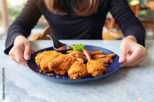 Closeup image of a woman holding a plate of fried chicken and french fries in restaurant