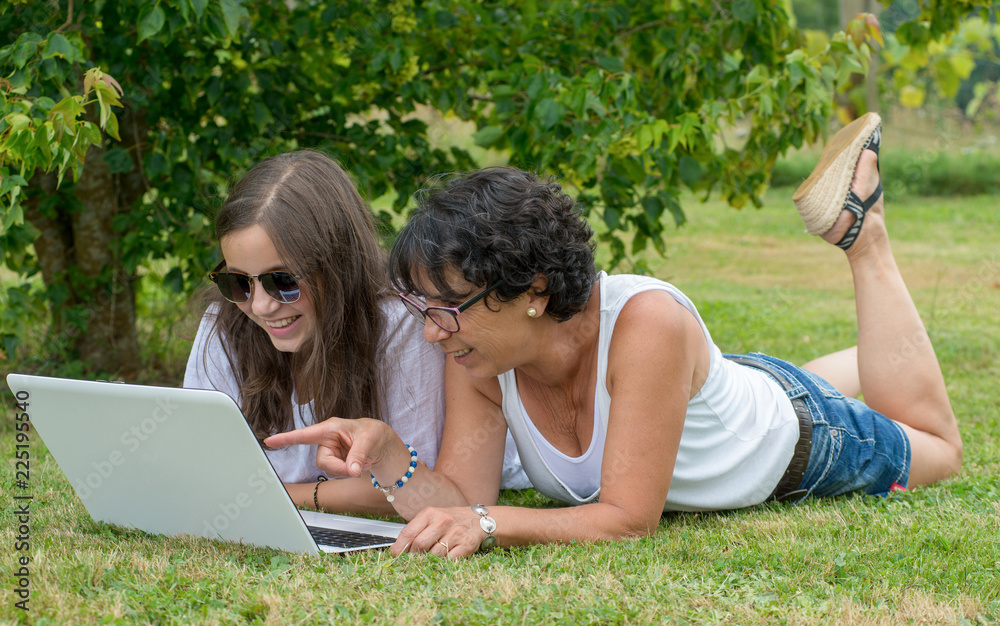 smiling mom and daughter using laptop at garden smiling mom and daughter using laptop at garden