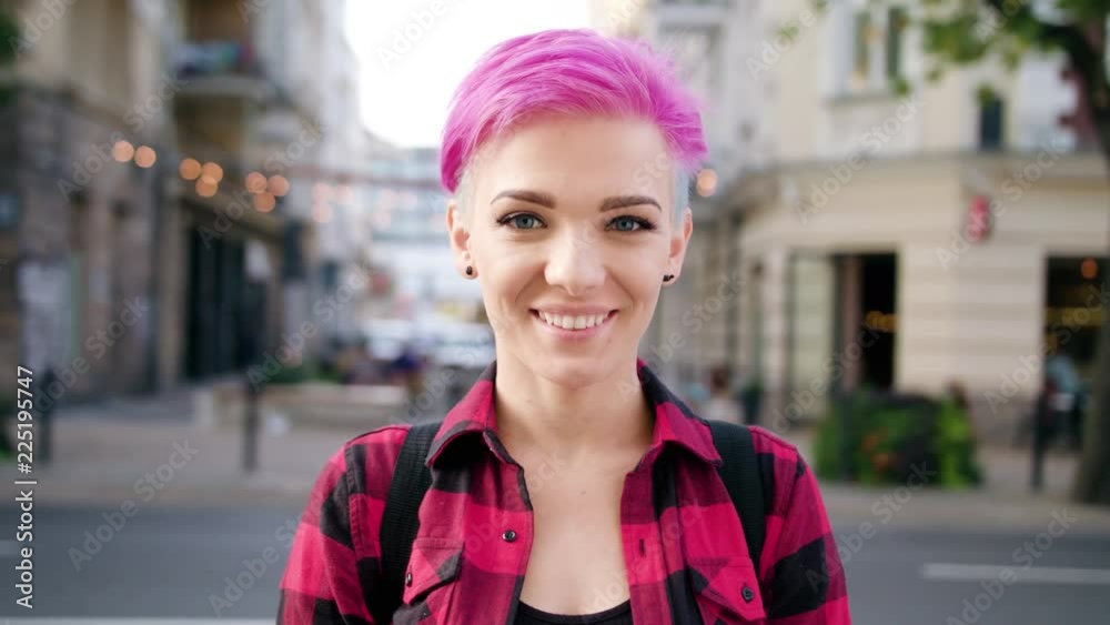 A happy smiling woman with a pink hair in the city street. Close-up shot. Soft focus A happy smiling woman with a pink hair in the city street. Close-up shot. Soft focus