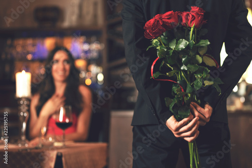 Fotografie, Obraz Romantic surprise concept - a man holding a bouquet of roses and wants to give it to a woman during dinner at a restaurant
