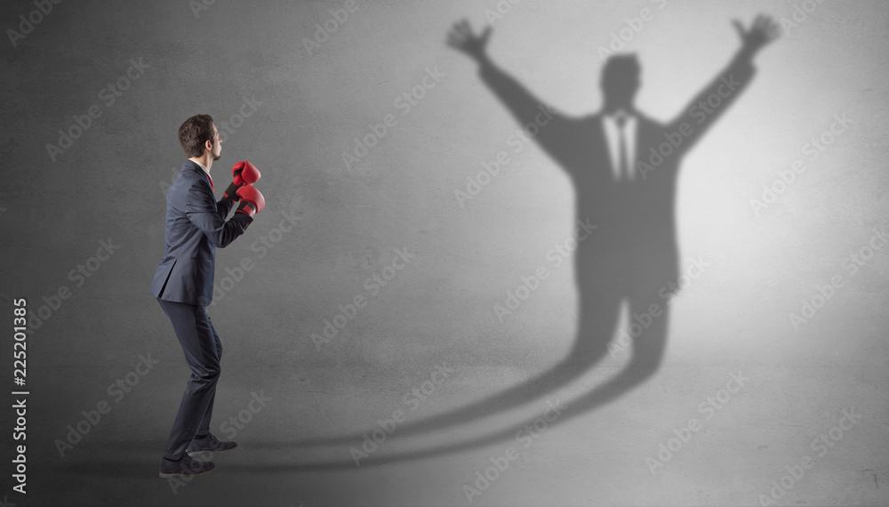 Businessman with boxing gloves fighting with disarmed businessman shadow
