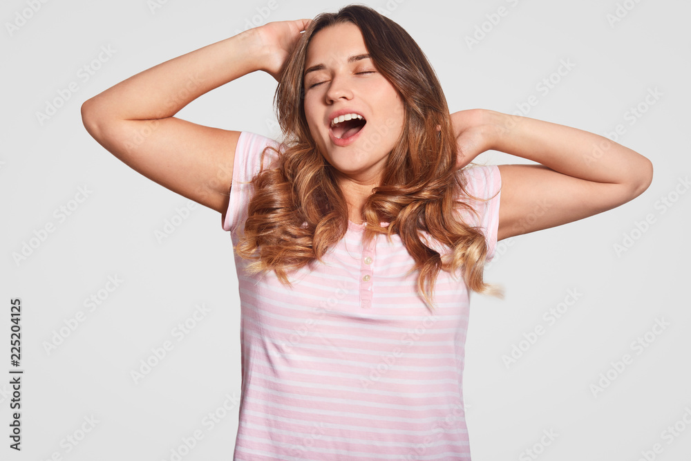 Bed time concept. Pleased woman had healthy sleep, stretches in morning, yawns, dressed in casual clothes, has long wavy hair, isolated over white background. Delighted sleepy girl in pyjamas Bed time concept. Pleased woman had healthy sleep, stretches in morning, yawns, dressed in casual clothes, has long wavy hair, isolated over white background. Delighted sleepy girl in pyjamas