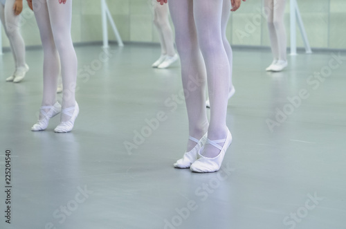 closeup legs of little ballerinas group in white shoes practicing in ballet school, slow motion. Young girls training classical dance exercise. Childhood, dancing, lifestyle concept