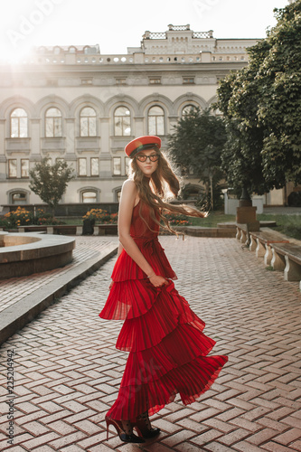 Young fashion woman in casual red dress, hat and glasses over urban city background autumn portrait. Hipster girl posing at street. Fashionable long hair model in elegant autumn clothes © oksana_bondar