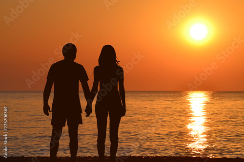 Young couple holding hands watching a sunrise at seashore © hibrida
