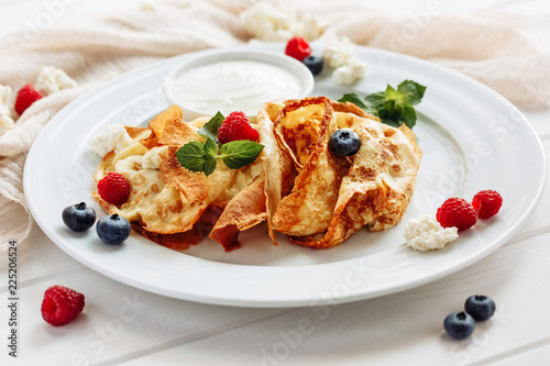 closeup of pancakes with cottage cheeseand strawberry, blueberry on plate on white plate background, decorated with mint leaves