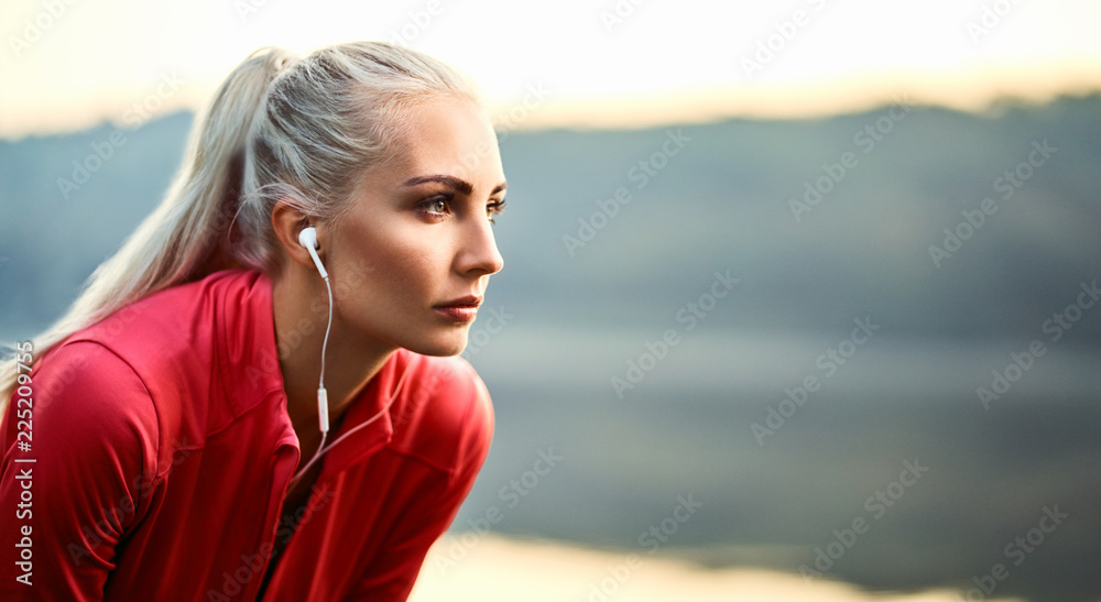 Beautiful young woman having rest and listening music outdoors during morning running exercise - obrazy, fototapety, plakaty 