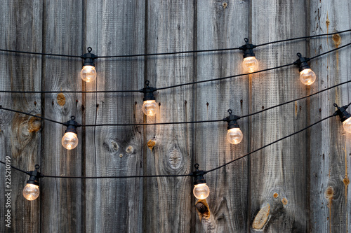 String of lights, yellow bulbs on old wooden background in the garden, copyspace, patio lighting decoration concept