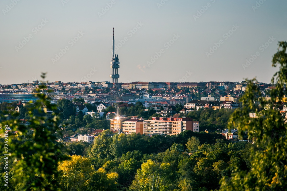 View of evening fall landscape of Czech republic capital city, Prague, Europe, famous tall observation tower at Zizkov, colorful houses, horizon in distance, grey blue sky, green trees in foreground